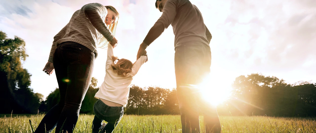 Familienspaß | © Studio Romantic Eltern schwingen ihr Kind an den Haenden auf einer Wiese
