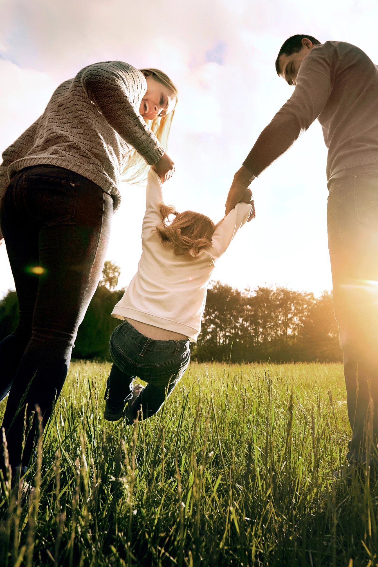 Familienspaß | © Studio Romantic Eltern schwingen ihr Kind an den Haenden auf einer Wiese