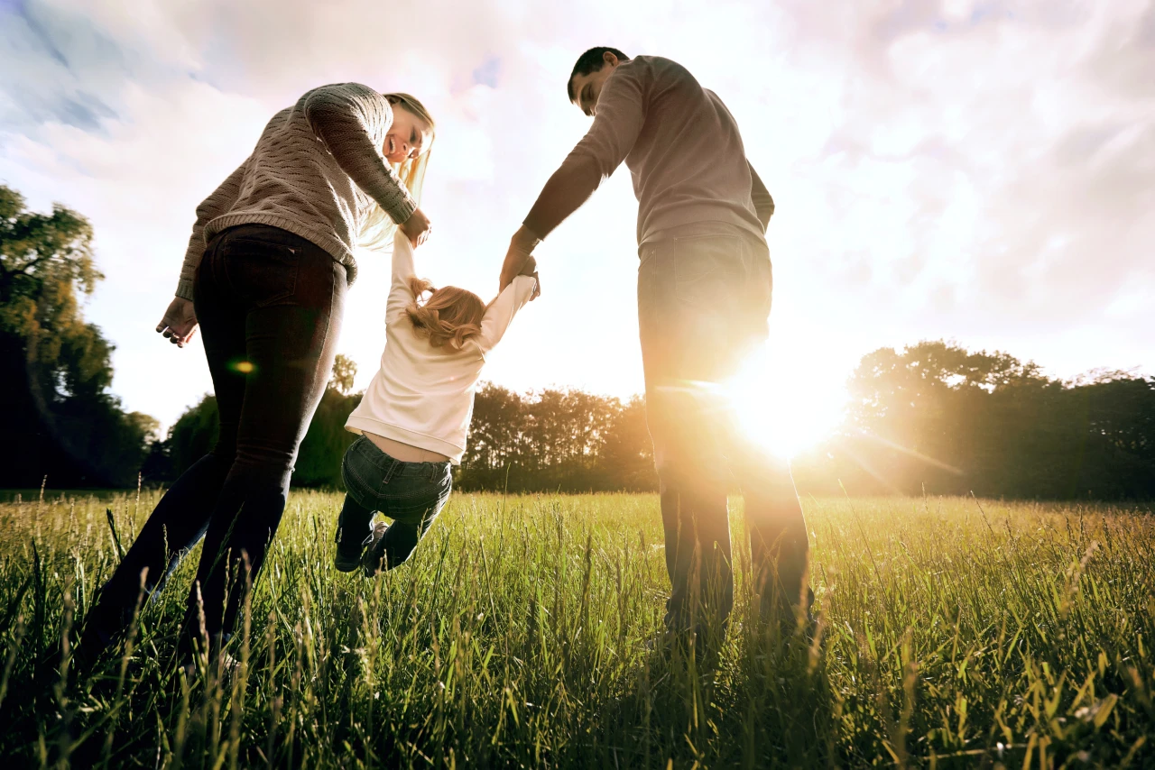 Familienspaß | © Studio Romantic Eltern schwingen ihr Kind an den Haenden auf einer Wiese
