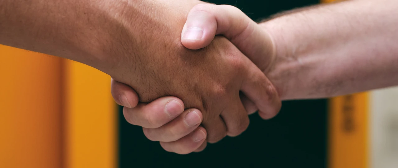 Handschlag | © KWB, Raphael Nast Nahaufnahme eines Handschlages und im Hintergrund sieht man einen KWB Kessel