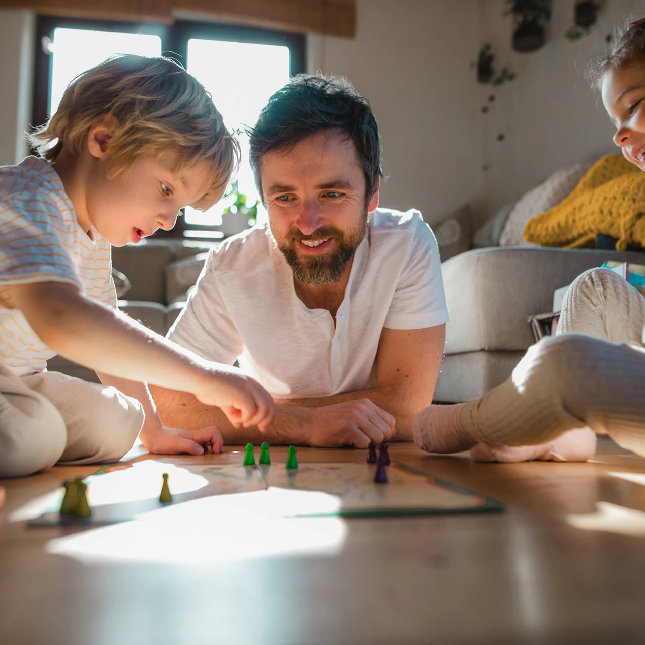© KWB, Halfpoint Ein Vater spielt mit seinen zwei Kindern ein Brettspiel auf dem Wohnzimmerboden.