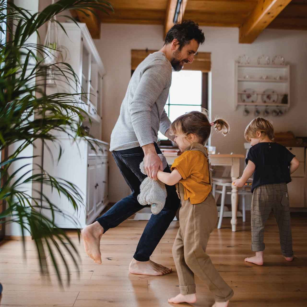 © KWB, Halfpoint Vater spielt barfuß mit zwei Kindern im Wohnzimmer, während sie gemeinsam lachen und herumtoben.