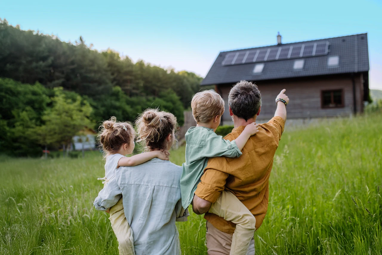 © KWB, Halfpoint Familie steht auf einer Wiese und blickt auf ein Haus mit Photovoltaikanlage auf dem Dach.