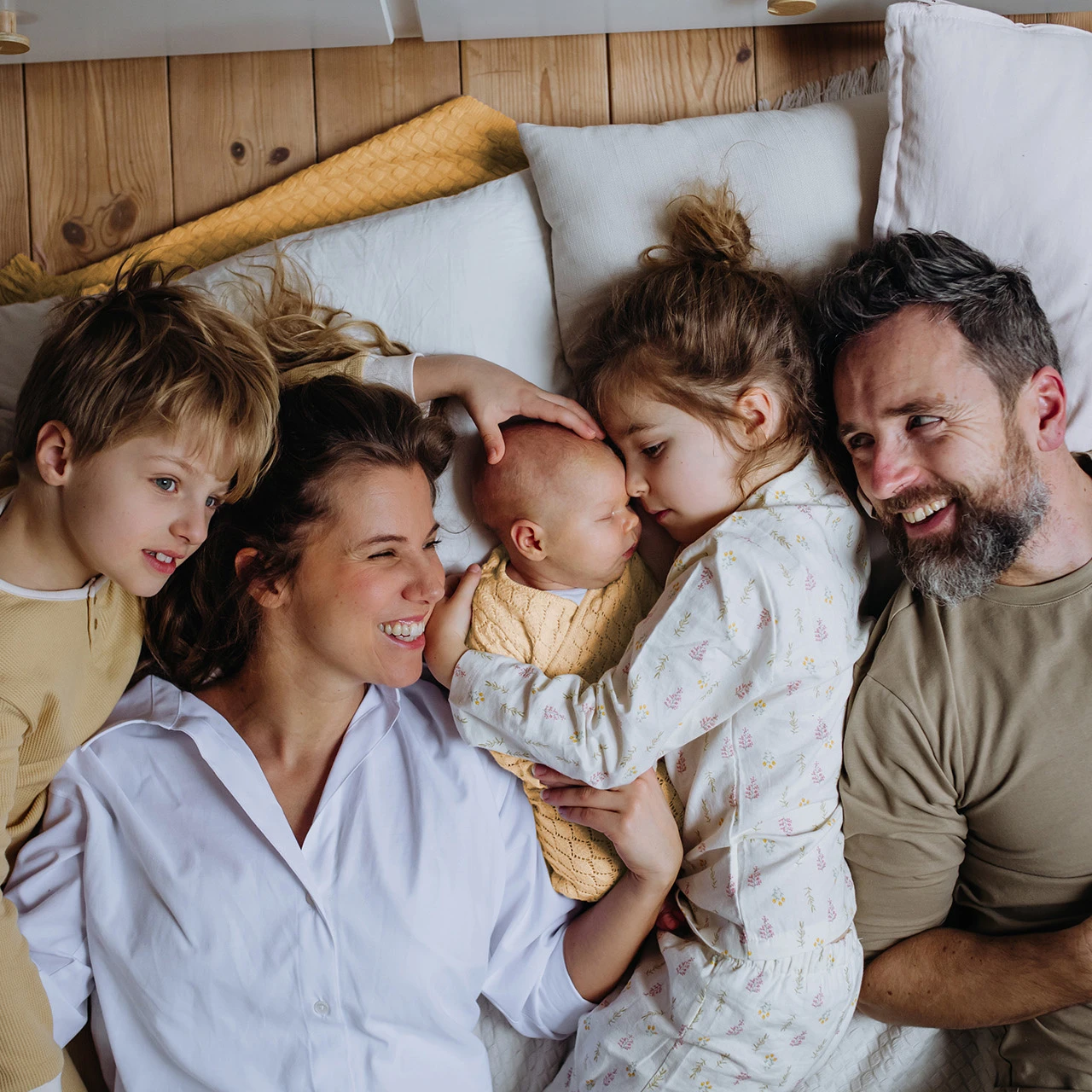 © KWB, Halfpoint Eine glückliche Familie liegt gemeinsam mit Kissen auf dem Boden.