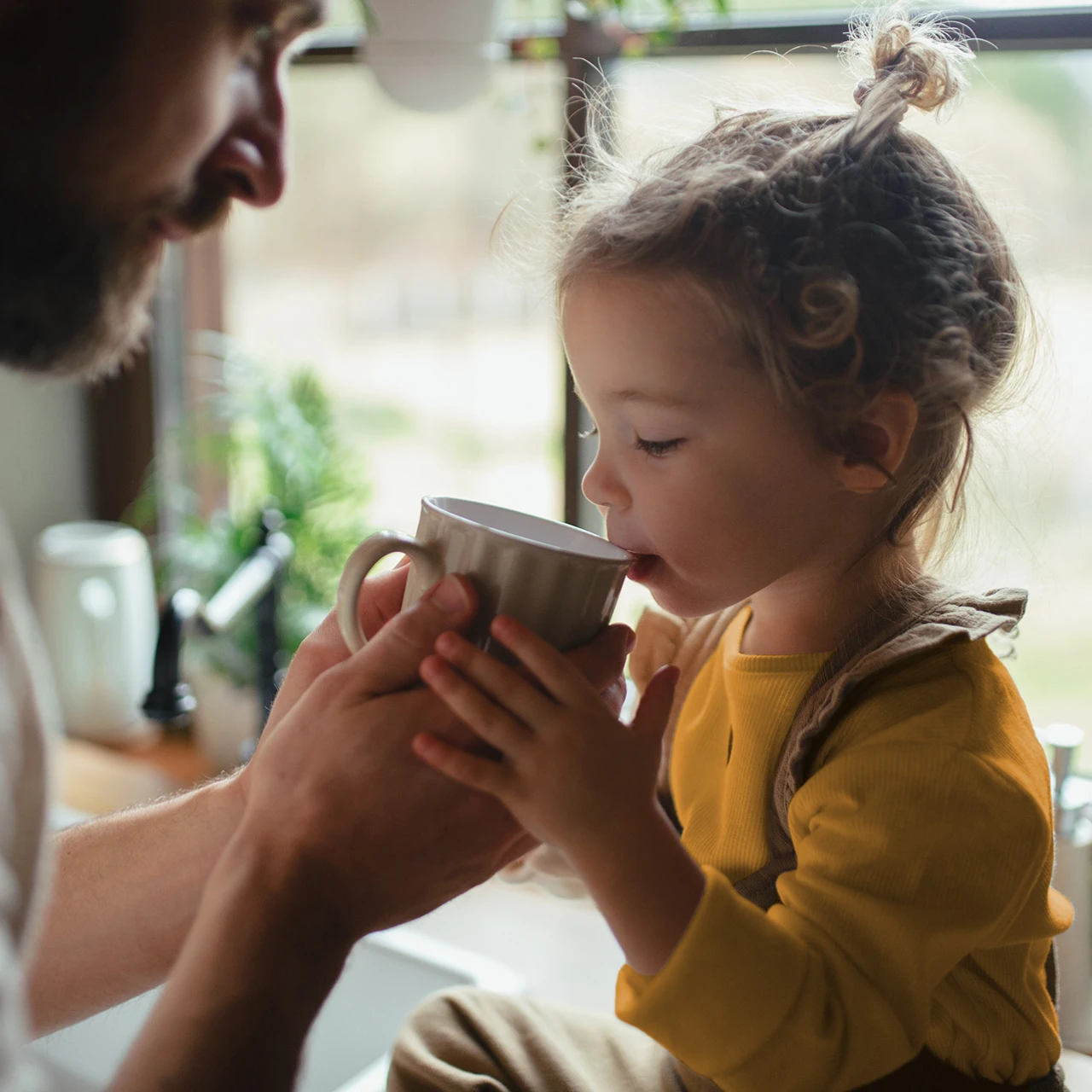© KWB, Halfpoint Ein kleines Kind trinkt aus einer Tasse, die vom Vater gehalten wird.