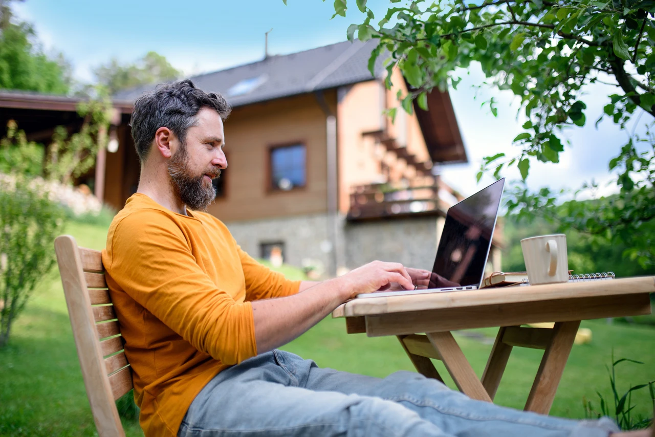 © KWB, Halfpoint Mann sitzt gemütlich auf Gartenmöbeln und arbeitet am Laptop.
