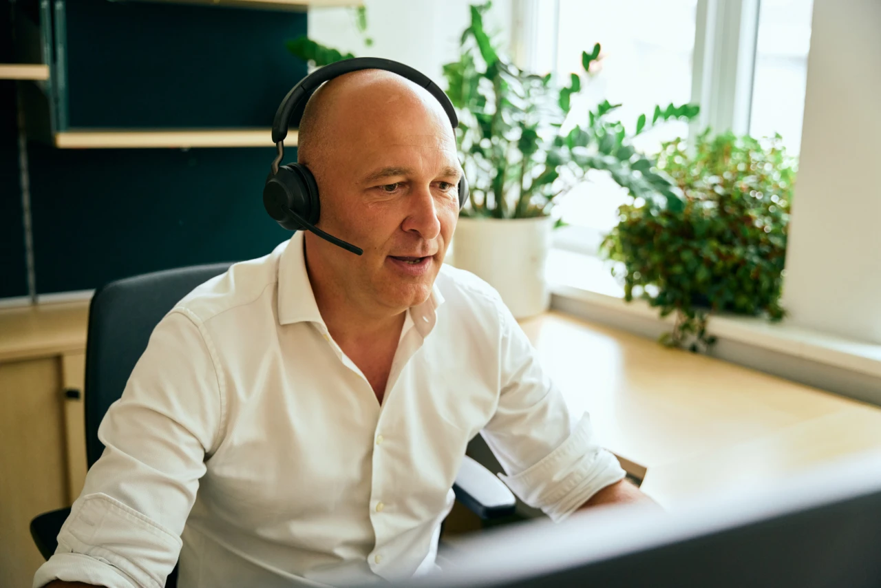 © KWB, Raphael Nast Mann arbeitet mit Headset auf dem Kopf am Schreibtisch.
