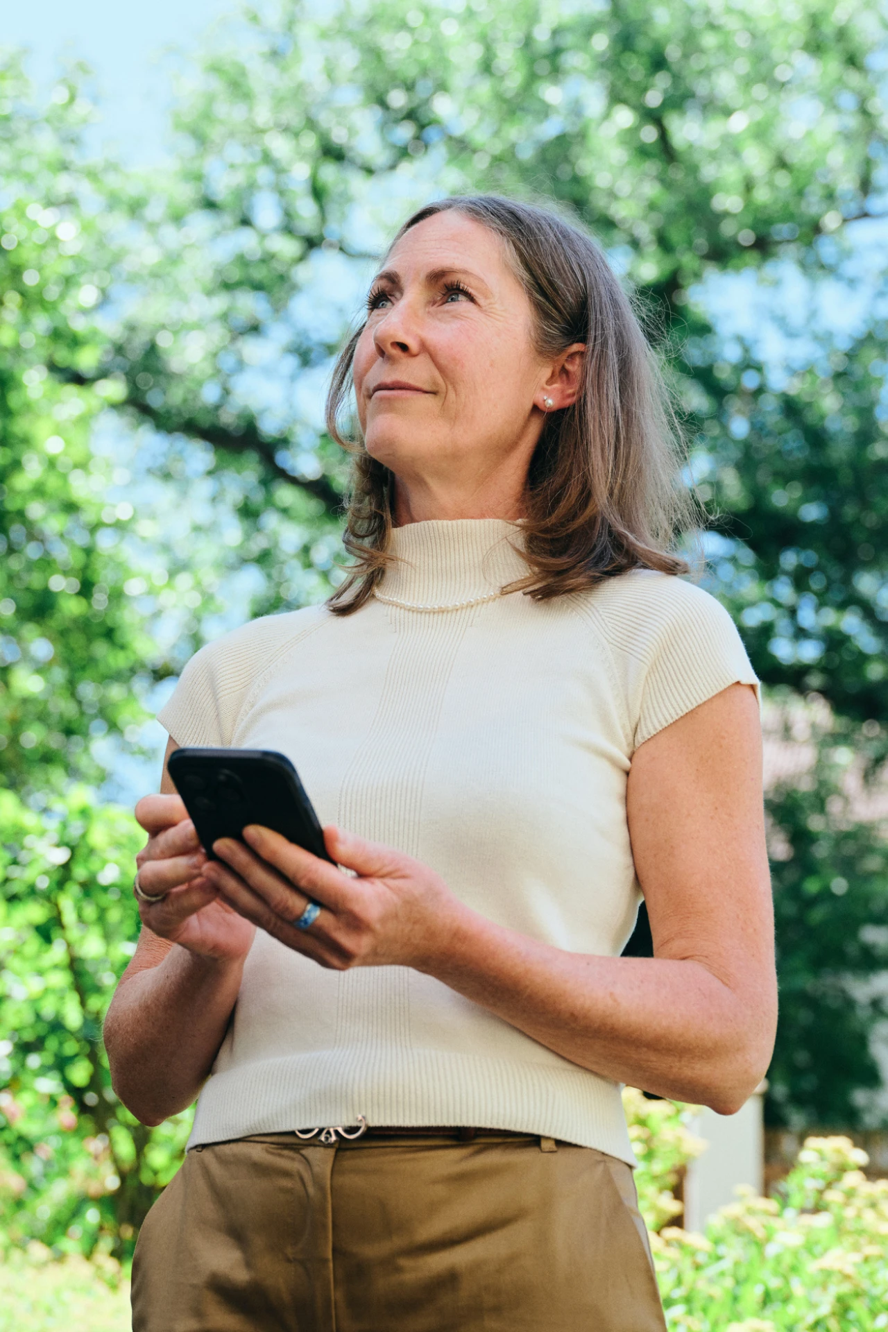 Referenzkunde Antje Krause | © KWB, Raphael Nast Man sieht eine Frau die ein Handy in der Hand haltet und in die Natur sieht
