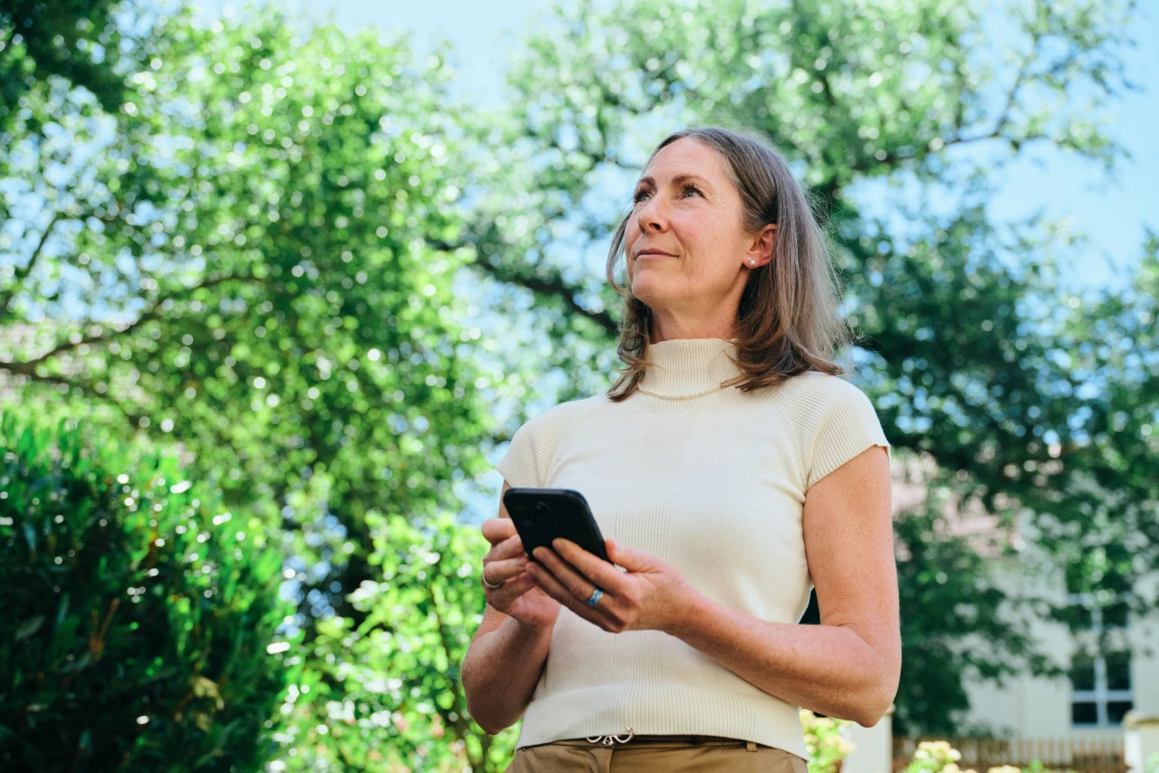 Referenzkunde Antje Krause | © KWB, Raphael Nast Man sieht eine Frau die ein Handy in der Hand haltet und in die Natur sieht
