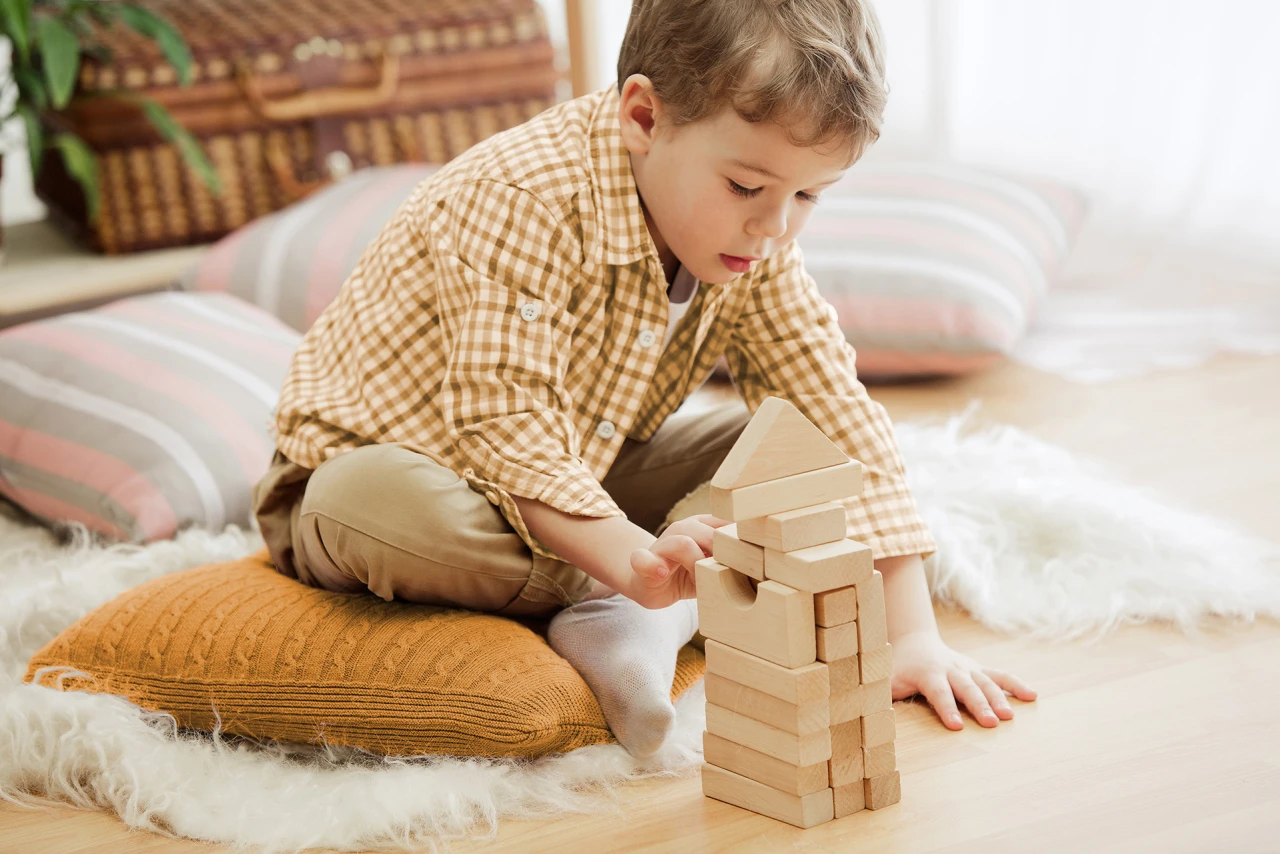 © KWB Junger Bub spielt auf Fußboden mit Holzbausteinen