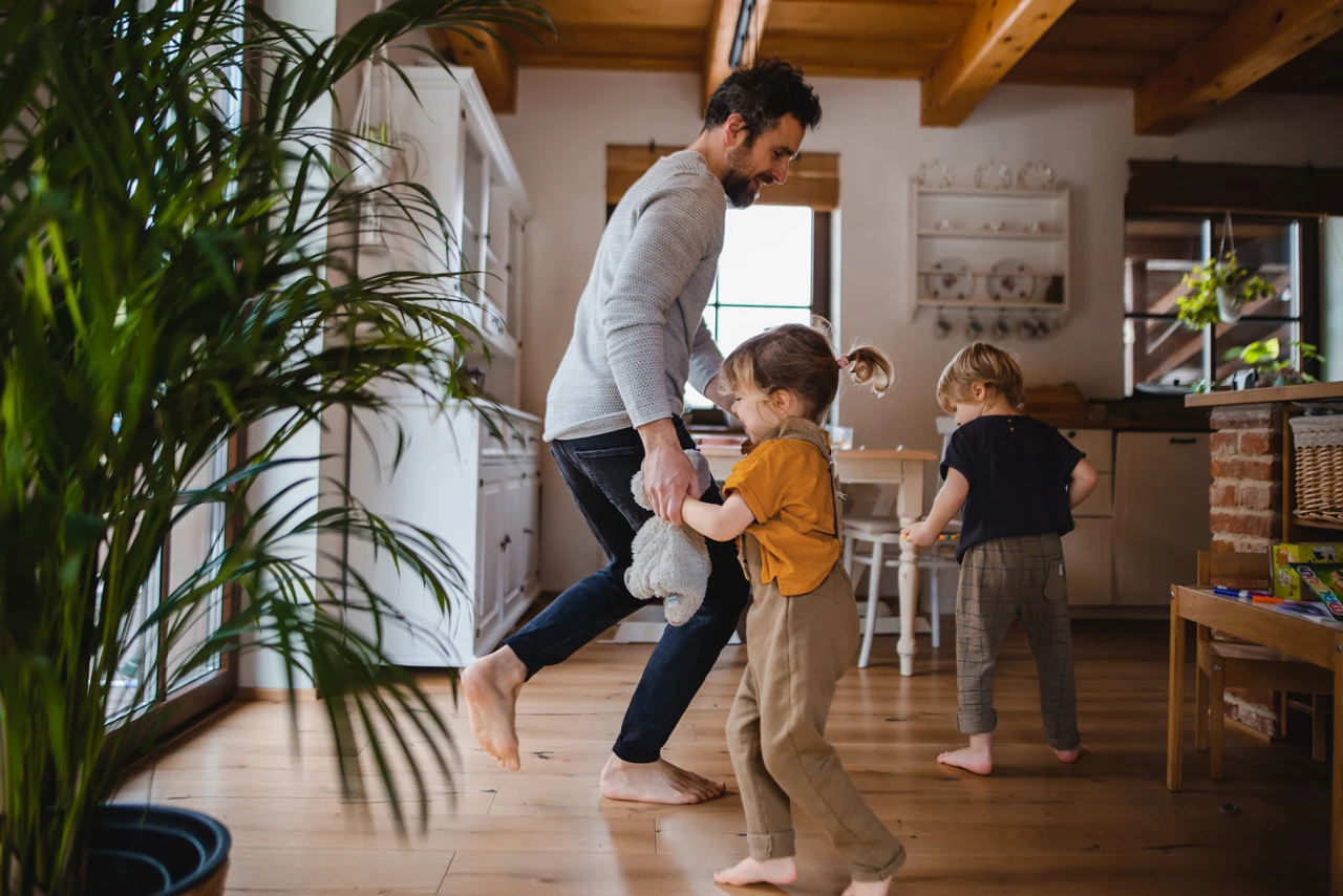© KWB, Halfpoint Vater spielt barfuß mit zwei Kindern im Wohnzimmer, während sie gemeinsam lachen und herumtoben.