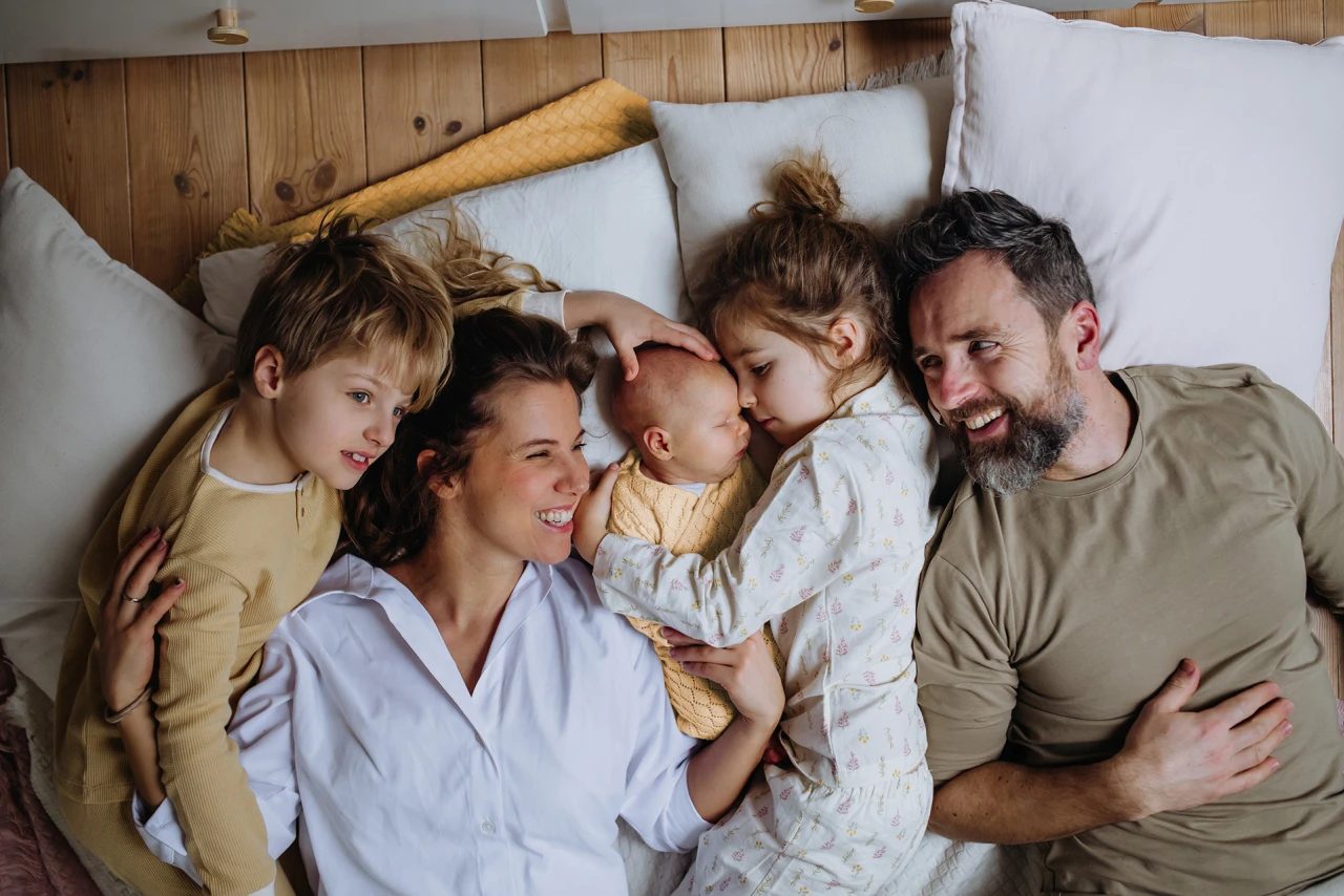 © KWB, Halfpoint Eine glückliche Familie liegt gemeinsam mit Kissen auf dem Boden.