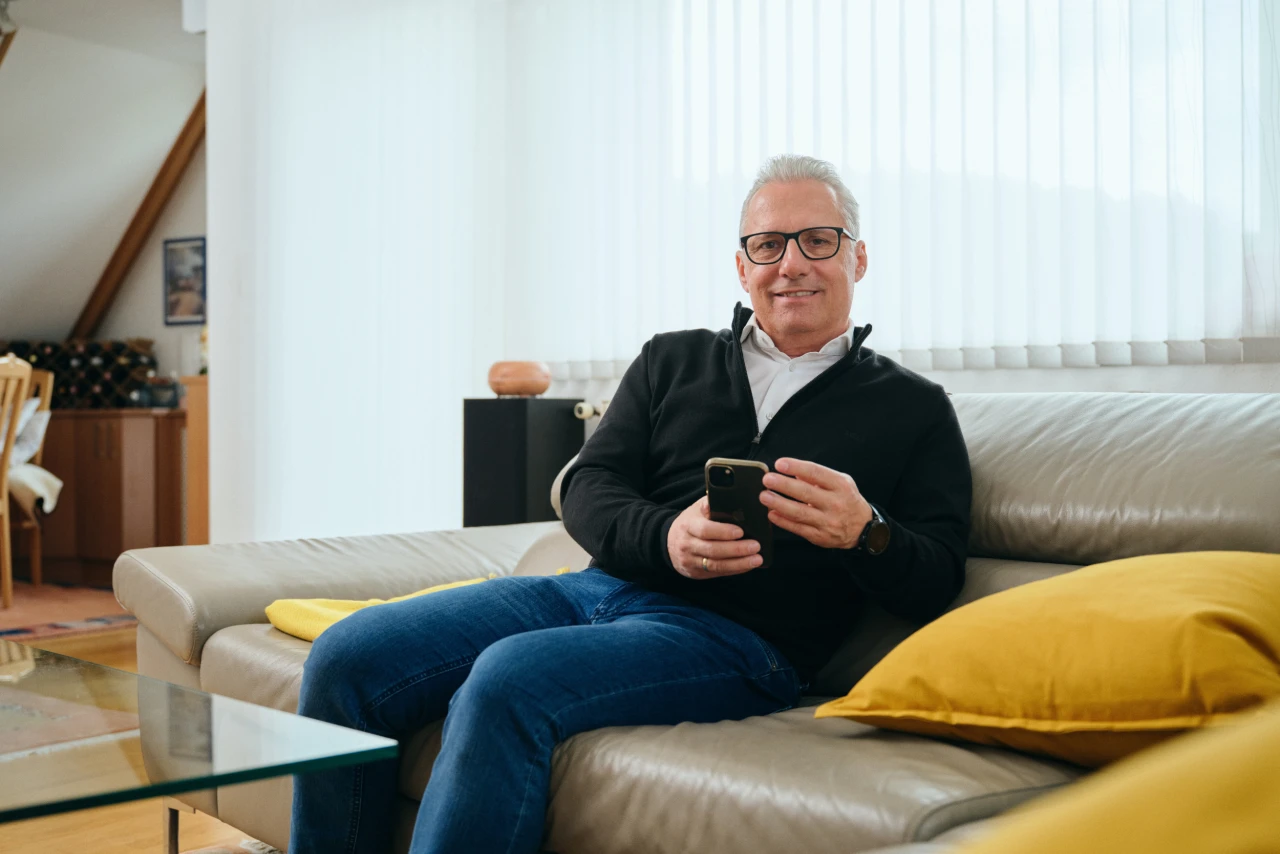 Referenzkunde Martiner | © KWB, Raphael Nast Hier sieht man Herrn Nast auf seinem Sofa und er haelt sein Handy