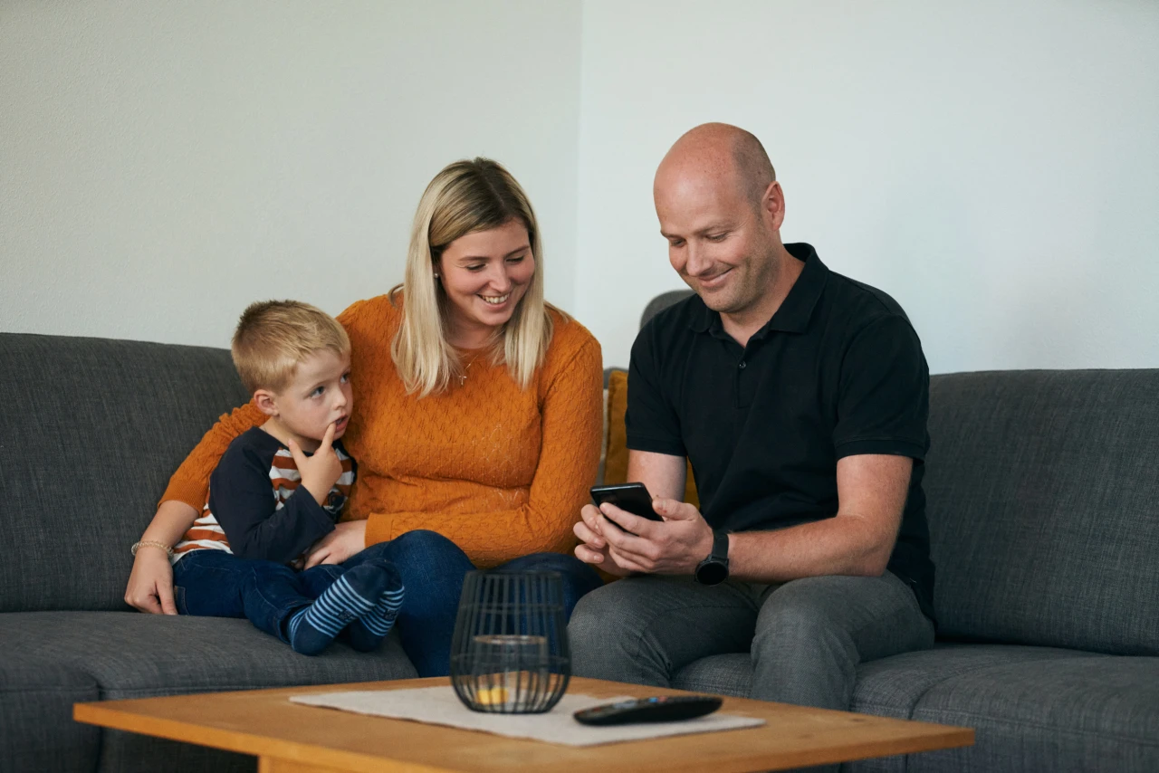 © KWB, Raphael Nast Familie Schmidbauer sitzt auf Couch und blickt auf Smartphone
